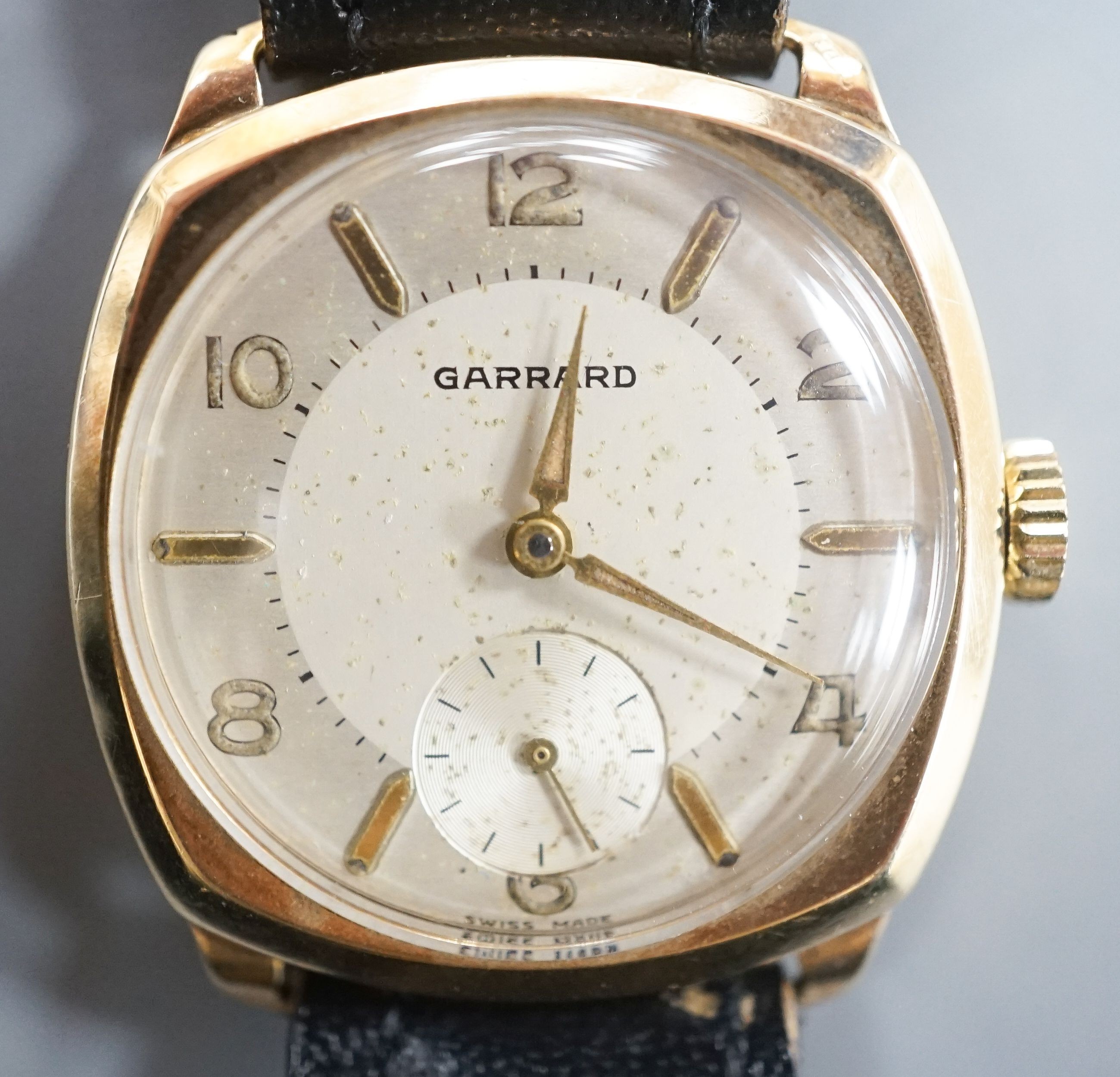 A gentleman's 9ct. gold wristwatch by Garrard in cushion case, silvered dial, baton and Roman numerals, Swiss 16 jewel movement, c.1957 inscription to back, black leather strap, cased diameter, 30mm, gross 24 grams.